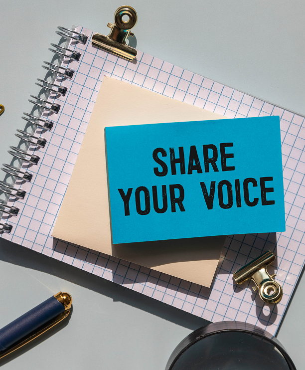 Paper note with "Share Your Voice" text written on a table.